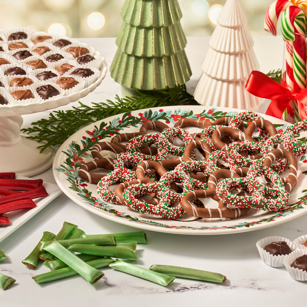 Decorative plate of chocolate covered pretzels with candy canes and Christmas trees in the background.