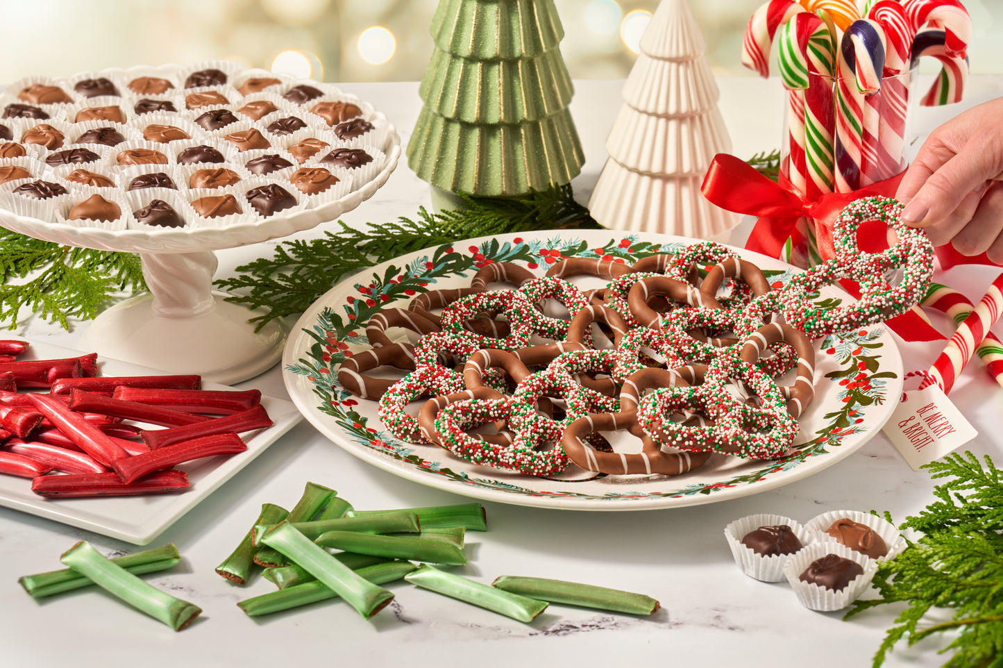 Decorative plate of chocolate covered pretzels with candy canes and Christmas trees in the background.
